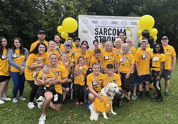 A group of people in gold shirts with a dog in the front.