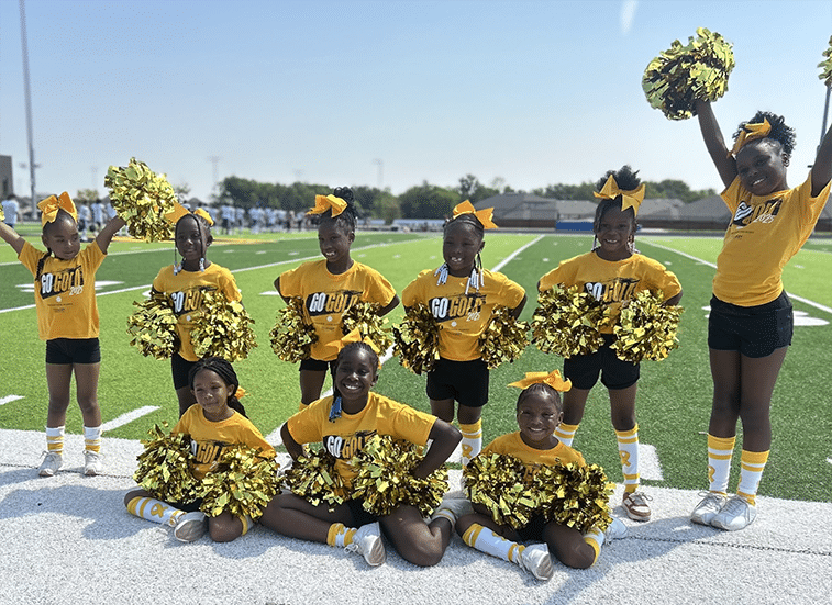 A photo of young girls cheerleading. They look grade school aged and all wear yellow shirts that say Go Gold on the front. They all have gold pompoms in their hands.