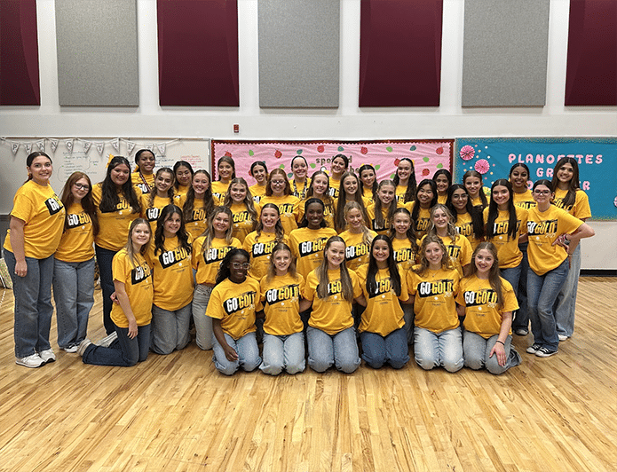 A group of children in three rows. The first two rows are seated and the third standing. They all wear yellow shirts that say Go Gold on the front.