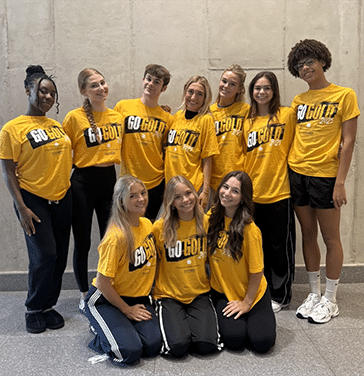 A group of children in two rows. The first is seated and the second standing. They all wear yellow shirts that say Go Gold on the front.