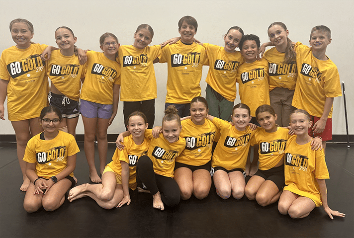 A group of children in two rows. The first is seated and the second standing. They all wear yellow shirts that say Go Gold on the front.