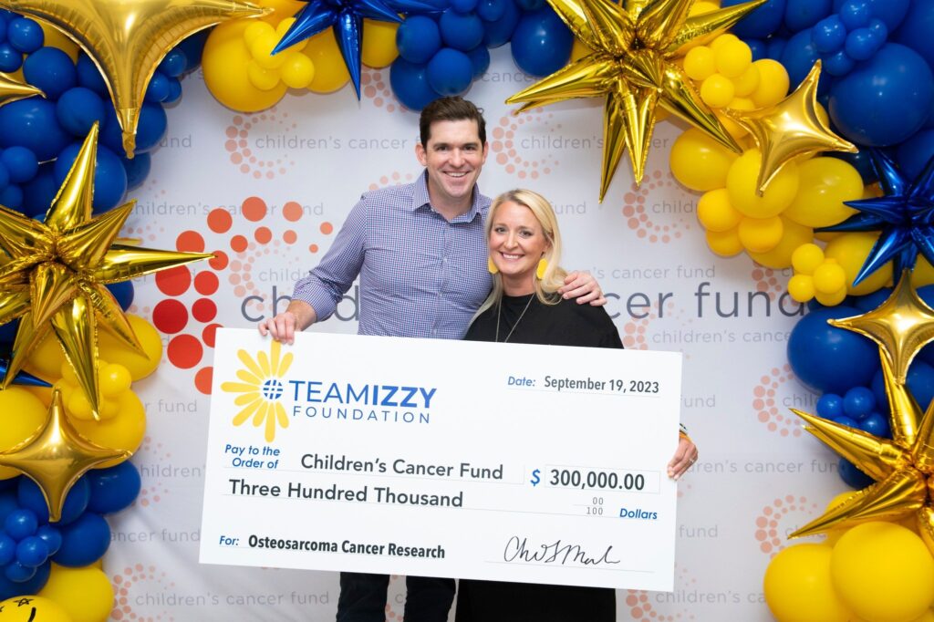 a man and a woman holding a giant check from Team Izzy Foundation to the Children's Cancer Fund