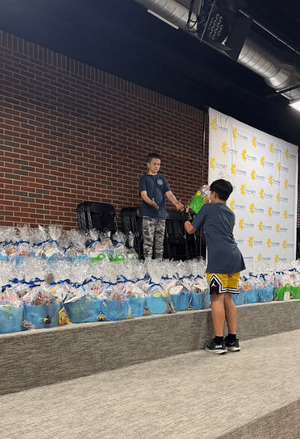 rowns of giftbags on a stage with two children handing the bags to each other