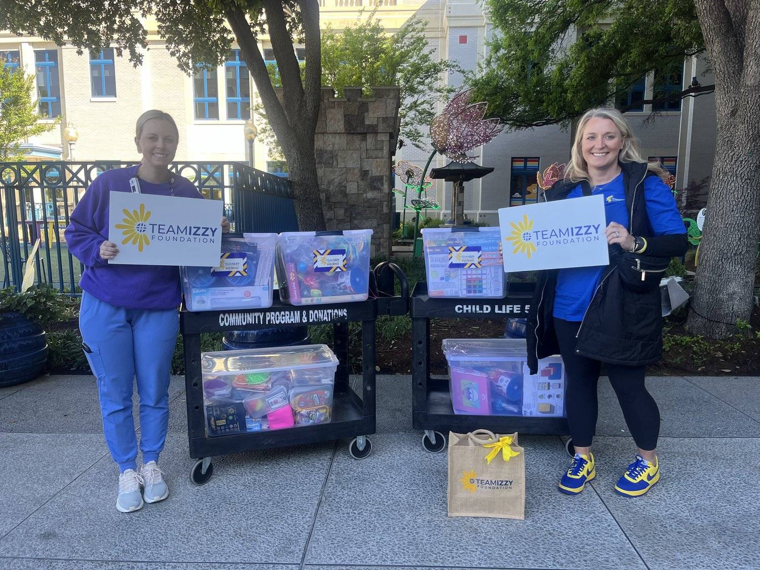 Two women standing outside holding TeamIzzy signs