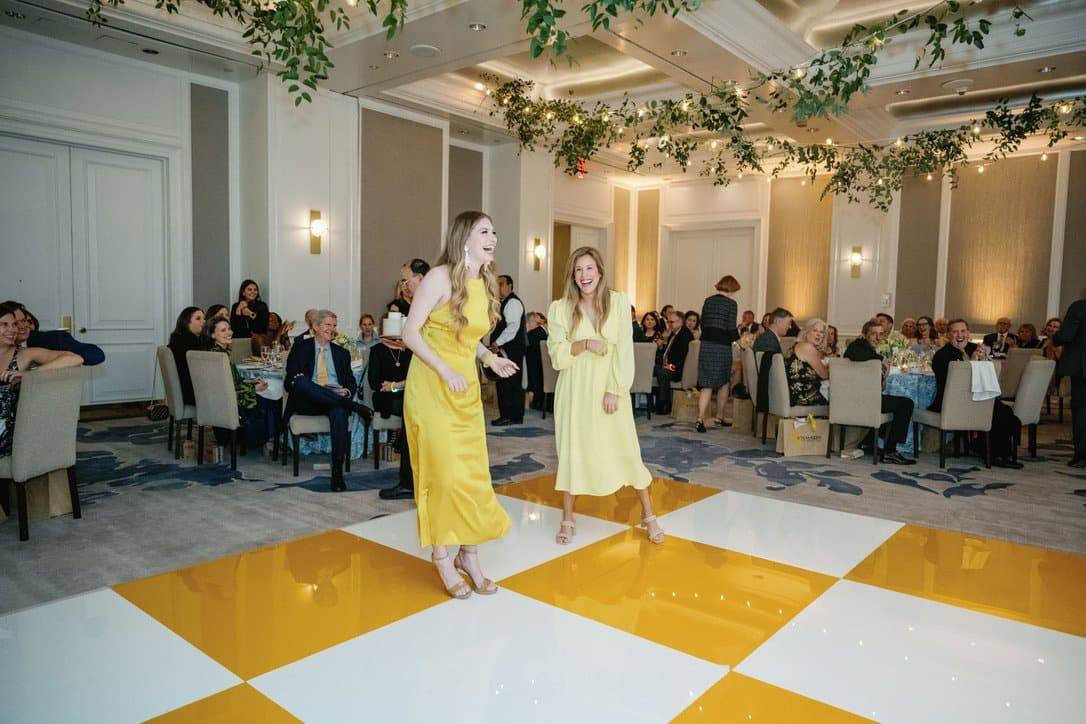 two women on a dance floor with a yellow and white tiled surface. The women wear yellow dresses