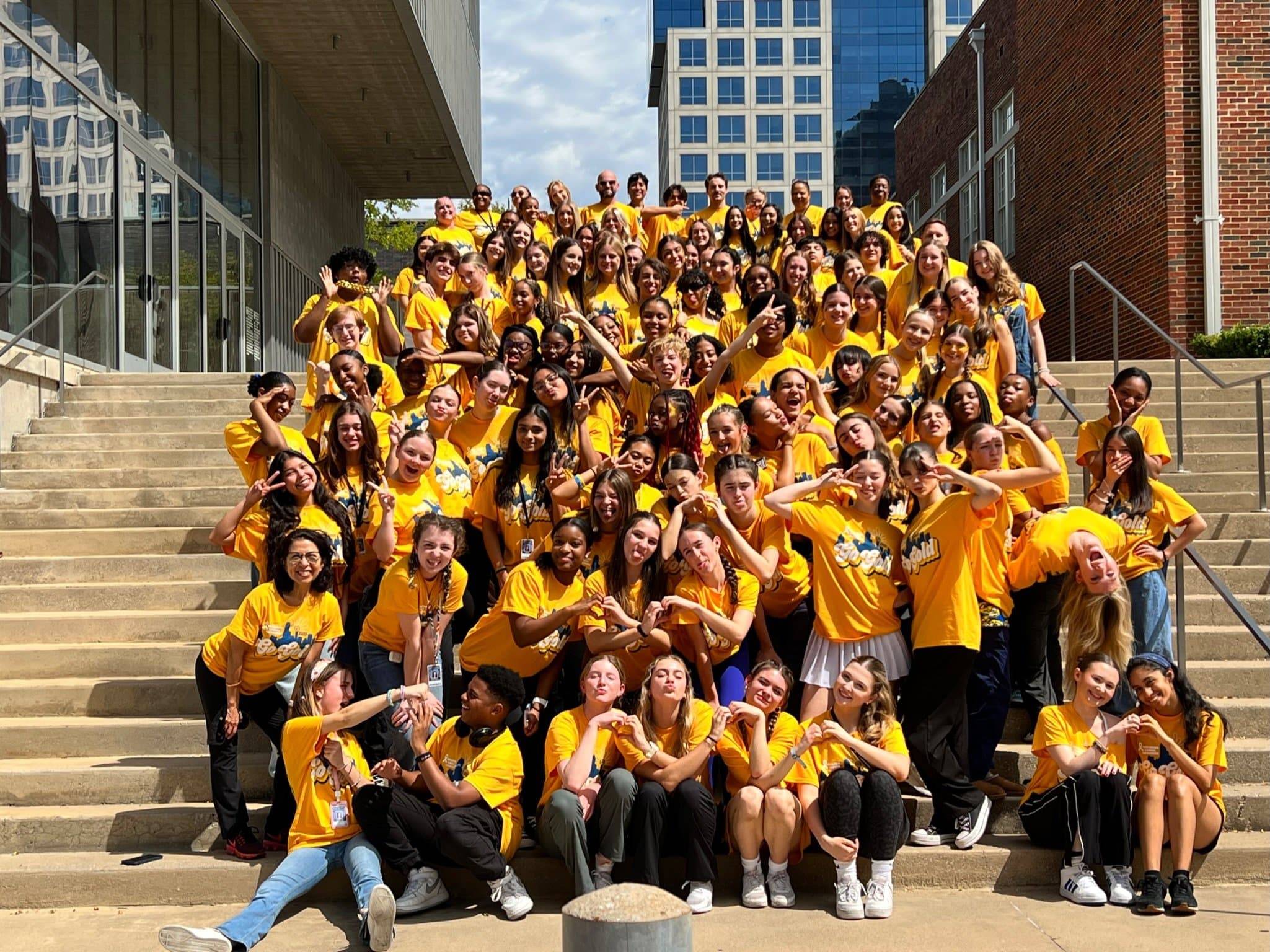 a large group of students in gold t-shirts sitting on steps