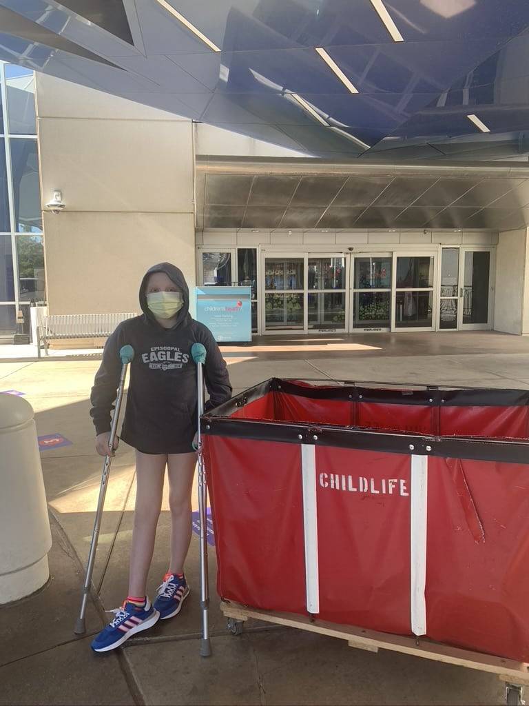 A child on Crutches standing next to a red bin that says "childlife" on it