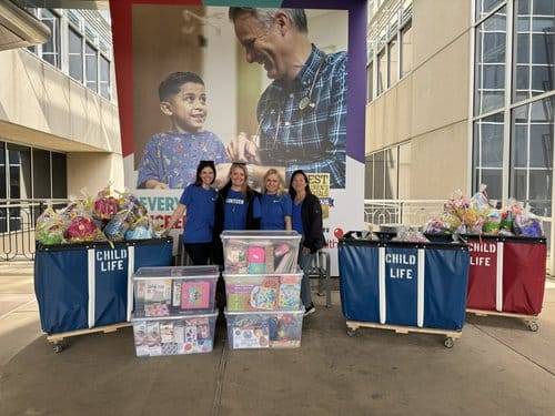 Four women standing near large bins that say Child Life on them