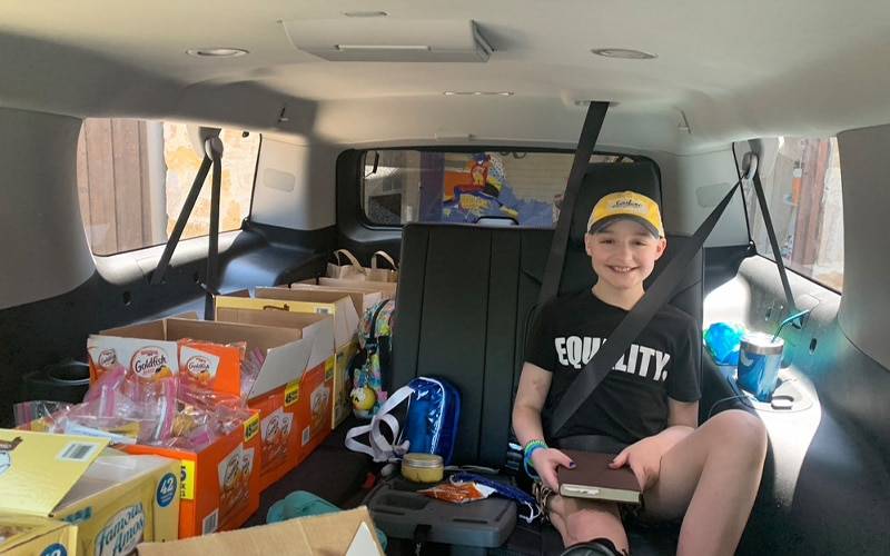 a smiling chiling in a vehicle with a bunch of boxes in the vehicle