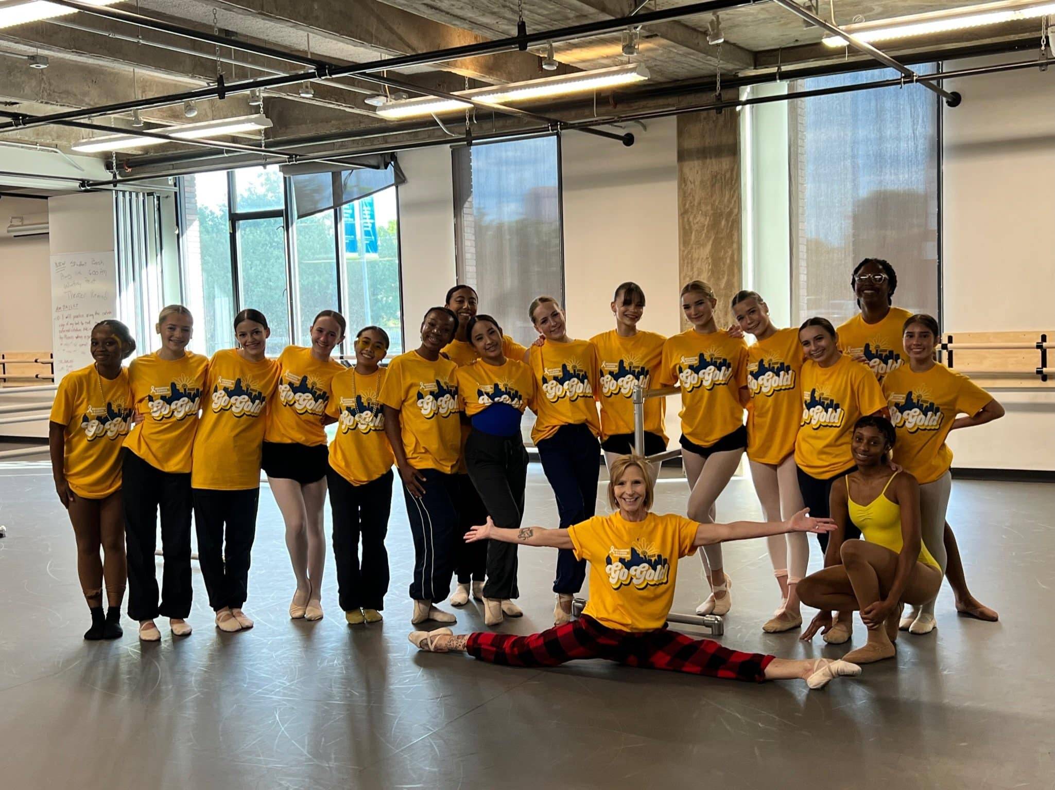 a group of kids in gold t-shirts in a gym with one child in the front doing the splits