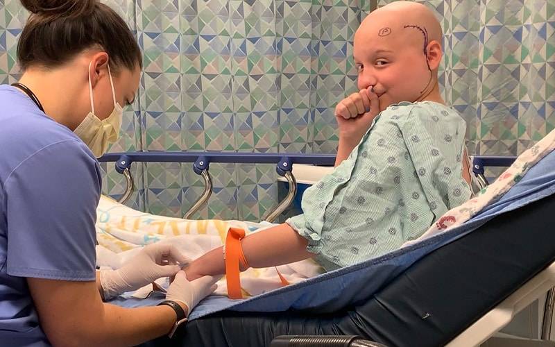 a child with no hair in a hospital bed being tended to by a nurse