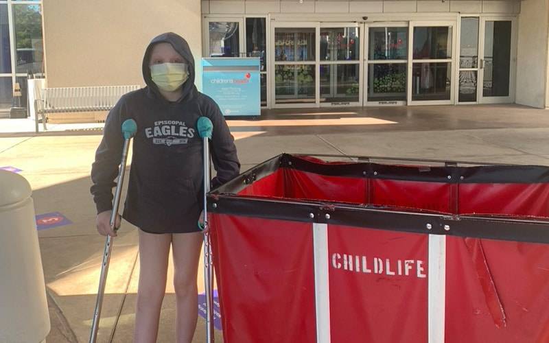 a child on crutches standing next to a red bin that says childlife on it